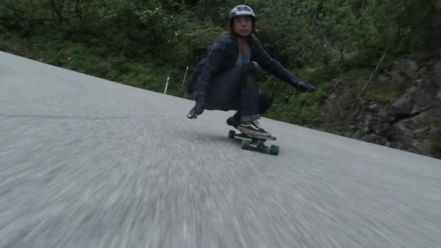 A skateboarder speeds down a mountain road