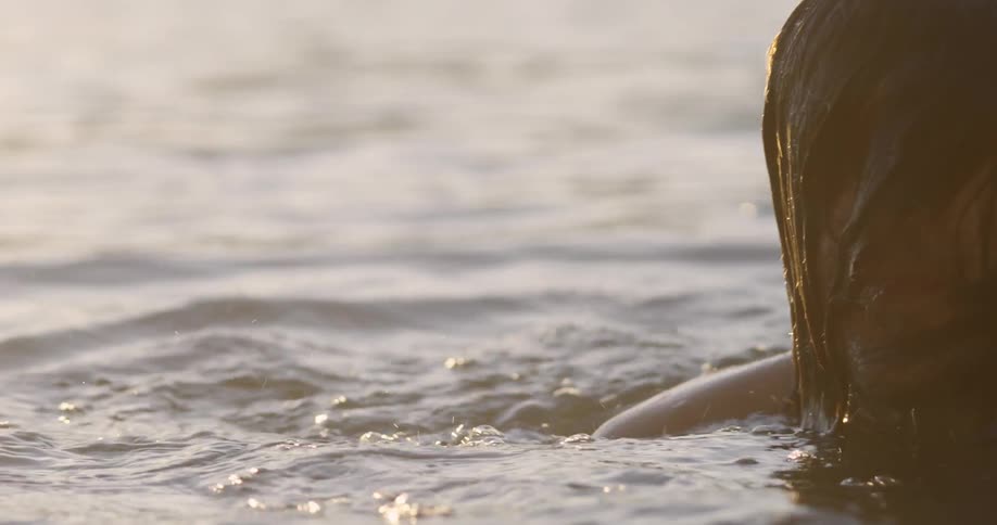 A man surfaces from beneath the water and brushes back his hair