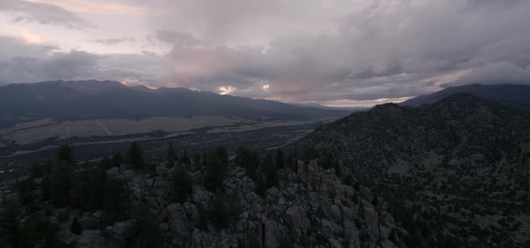 The sunset glows through clouds over hill tops