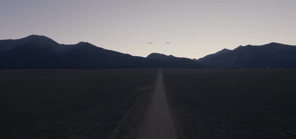 A dirt road leads to mountains at sunset