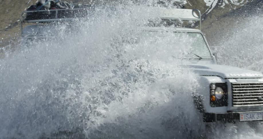 A land rover is driving through a river in a natural setting in slow motions