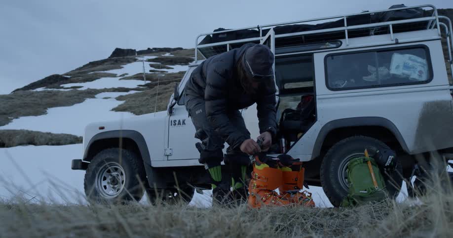 Man next to jeep ties shoes then picks up ski boots