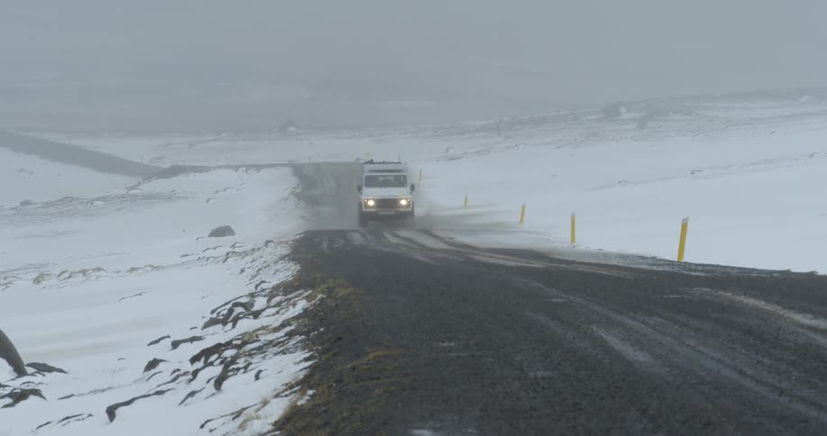 A vehicle drives down a snowy gravel road in storm