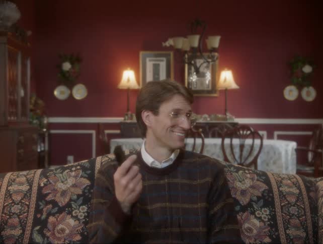 Man sits on a couch smiling and shaking his head