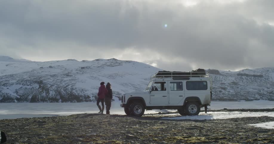A man and woman stand beside their suv and look out at a frozen lake