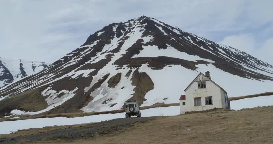 A white truck drives towards a house at the foot of a snowy mountain