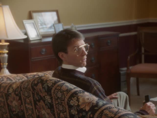 An upset girl walks through a living room and a man on a couch looks surprised