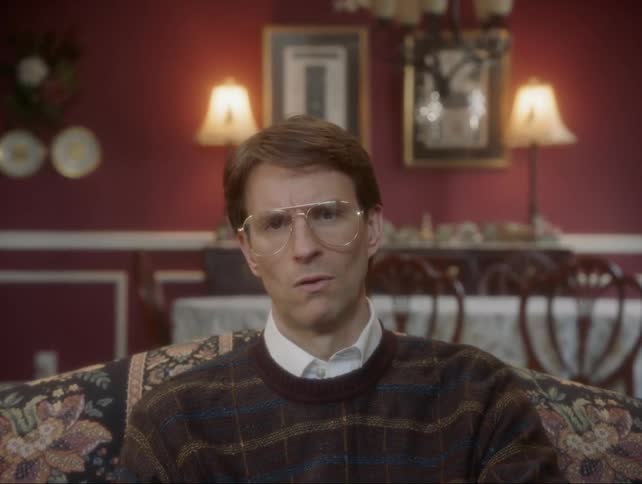 A man sitting on a couch makes skeptical facial expressions