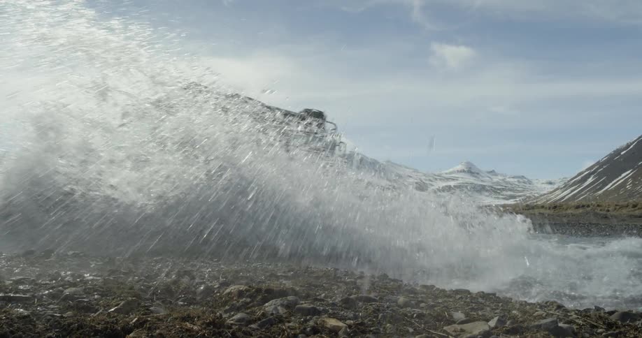 Jeep splashes through a stream surrounded by mountains