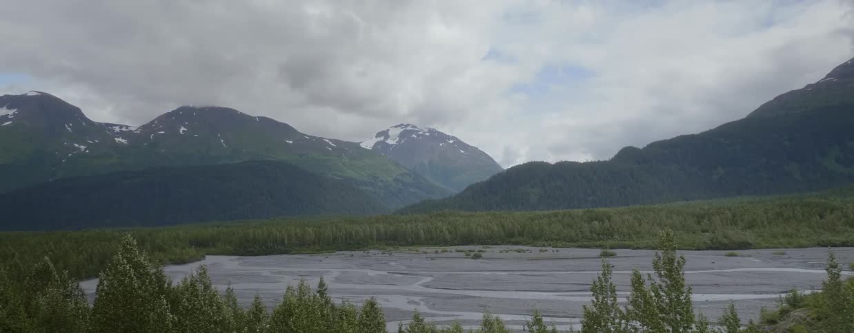 Trees ring a partially frozen lake near the mountains