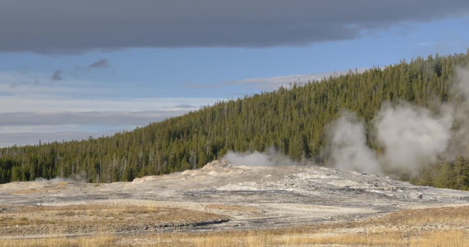 Smoke coming out of a small hill with a forest in the background