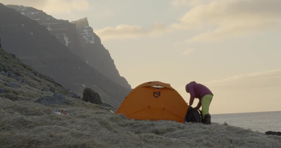 A woman stands next to a tent at sunset