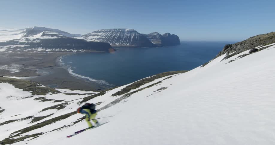 A woman is skiing down a mountain with the ocean in the distance