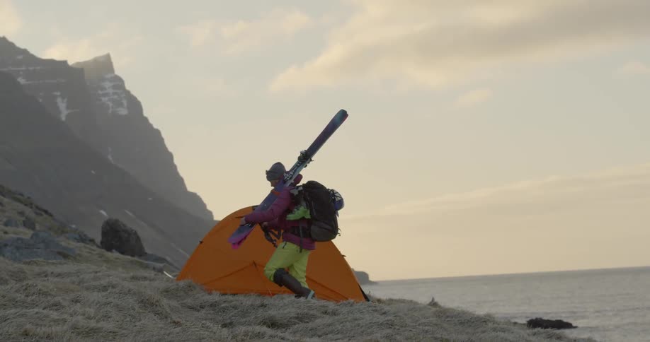 A woman walks towards a tent with skis over her shoulder