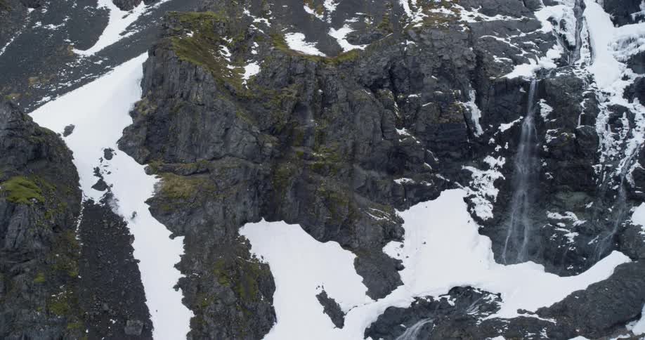 A small skier in vast landscape speeds down the snow with waterfall and birds