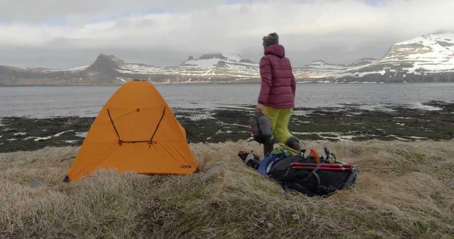 A woman takes a sleeping bag from her backpack and brings it into the tent