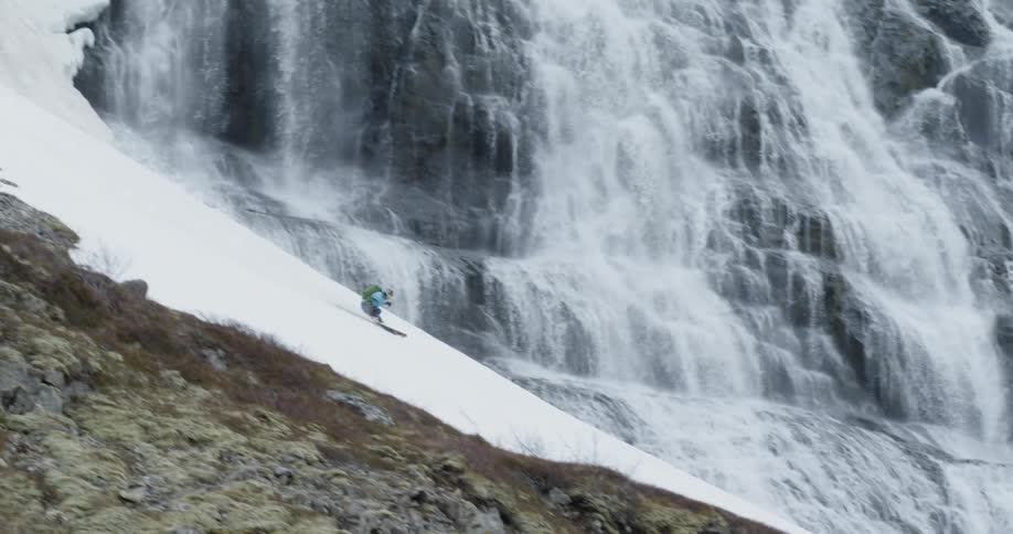 A skier glides down a mountainside near waterfalls