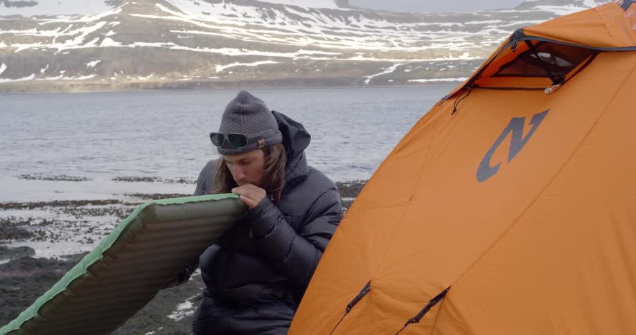 A man blows up an inflatable pad next to a tent
