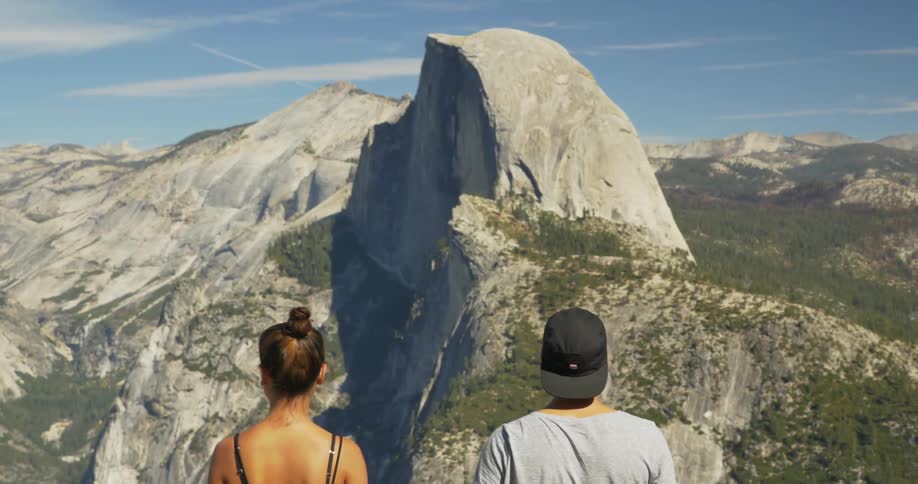 A couple stands looking out at half-dome in yosemite on a bright sunny day