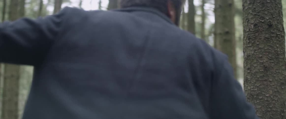 A man in a forest turns back and forth nervously during the day