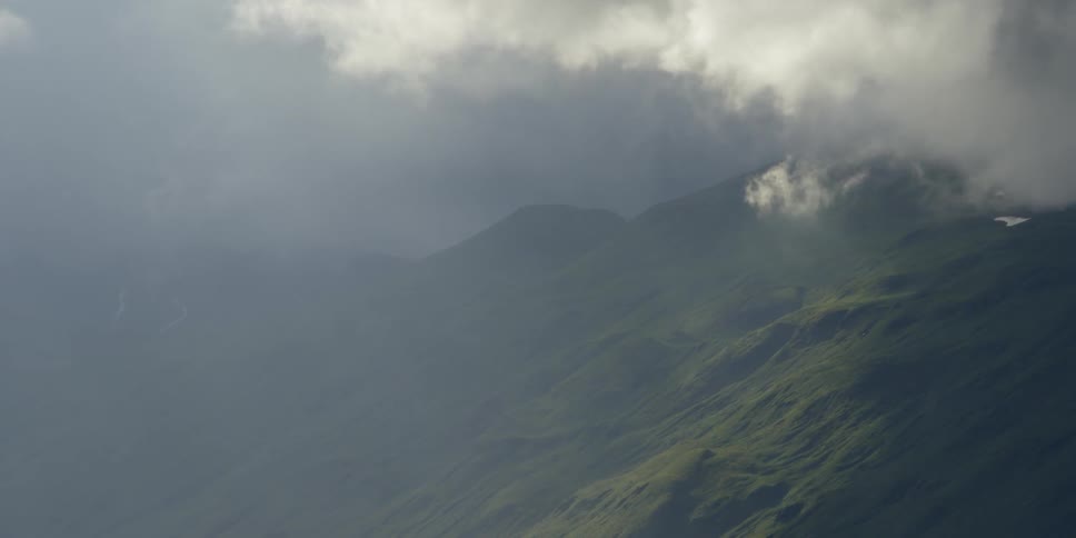 Clouds roll over a green mountain