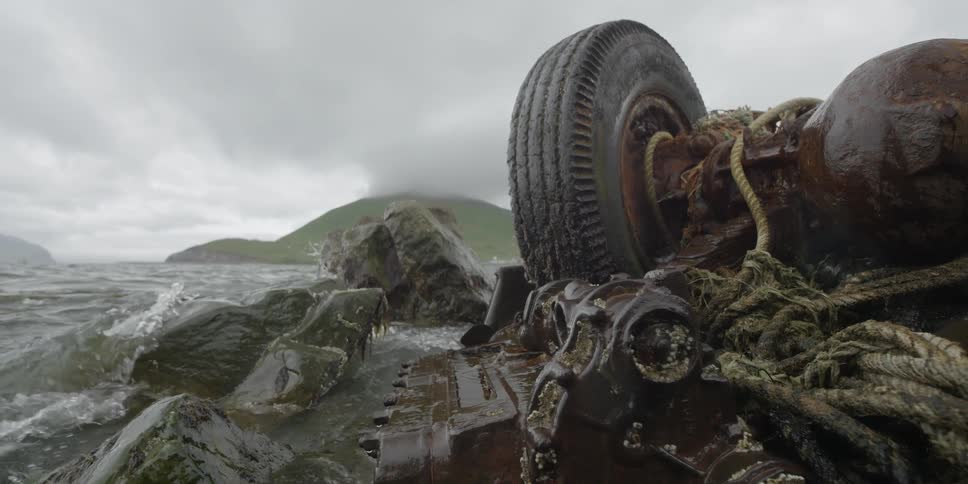 Rusted vehicle upside down at ocean's edge