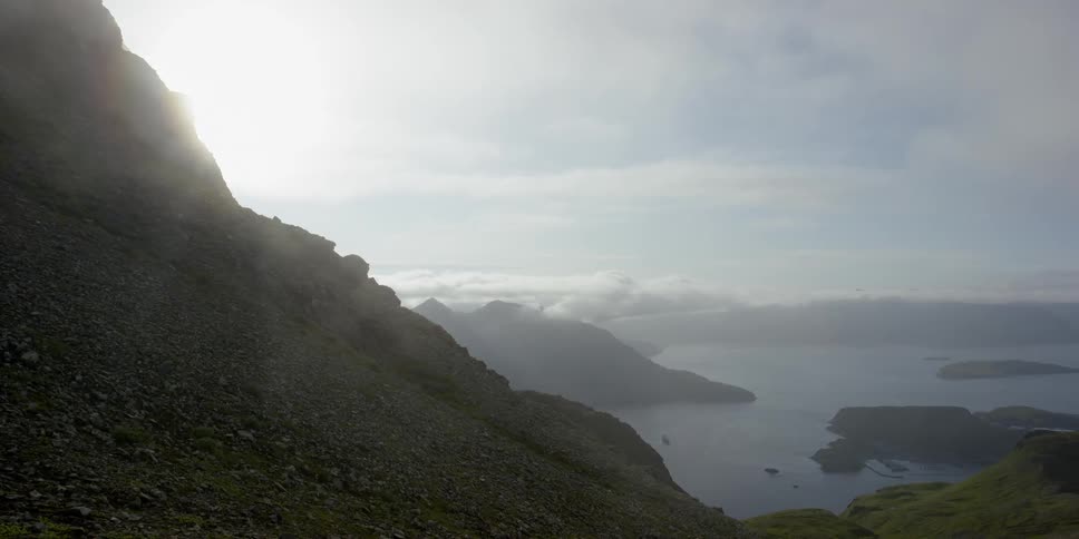 Clouds drift over a coastal area beyond mountains