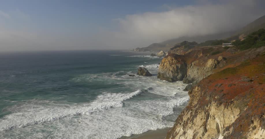 Waves crash onto a small beach below a cliff