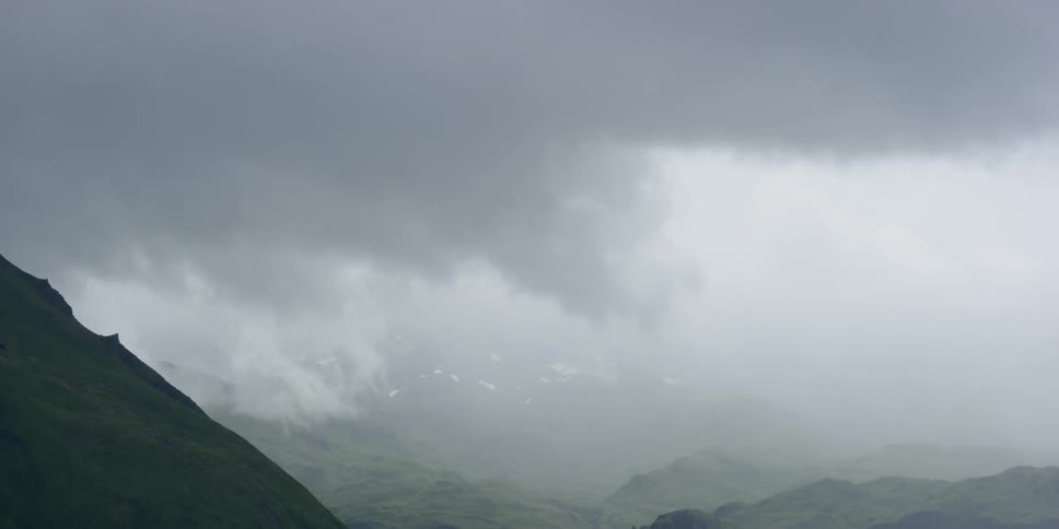 Clouds pass a grassy mountain peak