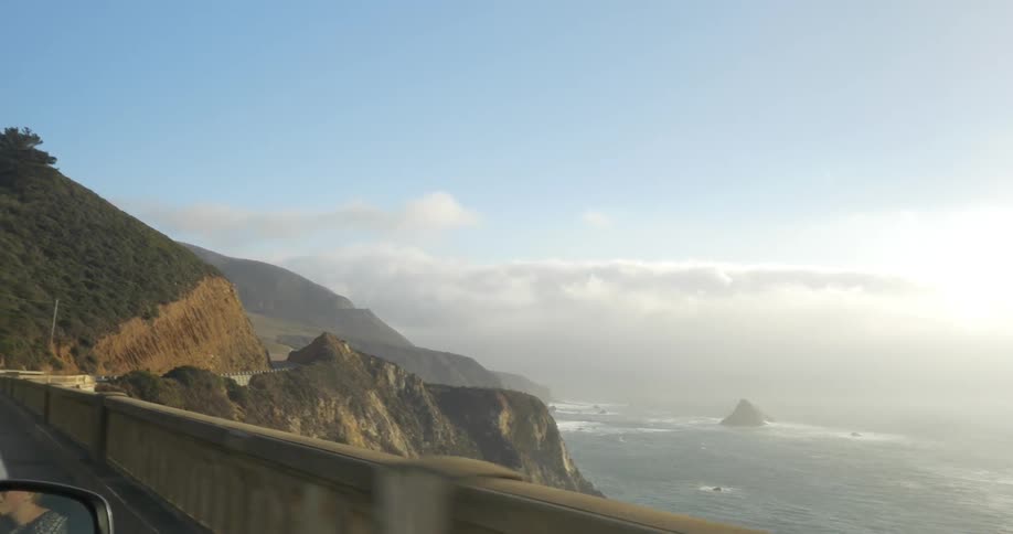 Inside view of a vehicle traveling along a highway on a cliff overlooking water