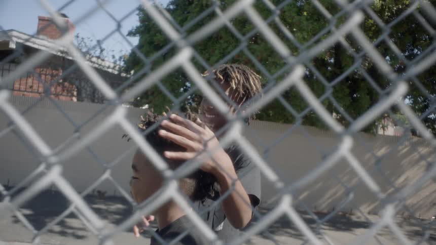 Two boys smile and hug as they walk near a fence in their neighborhood during the day