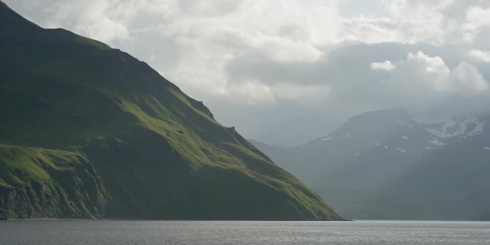 Clouds hang over green hills, ocean and mountains