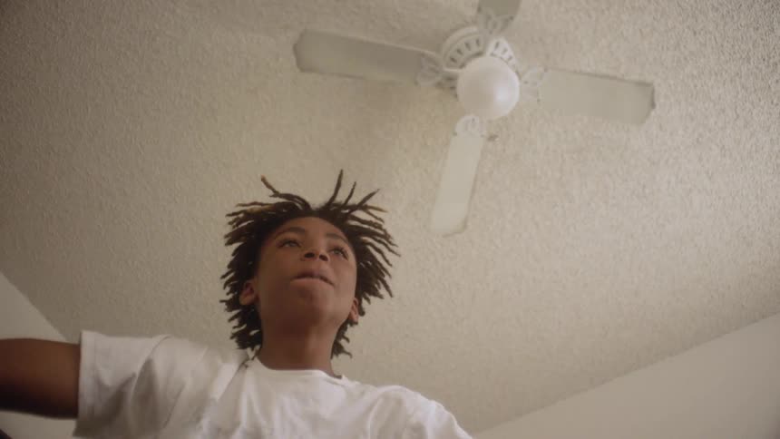 A kid is dancing in his room under a ceiling fan