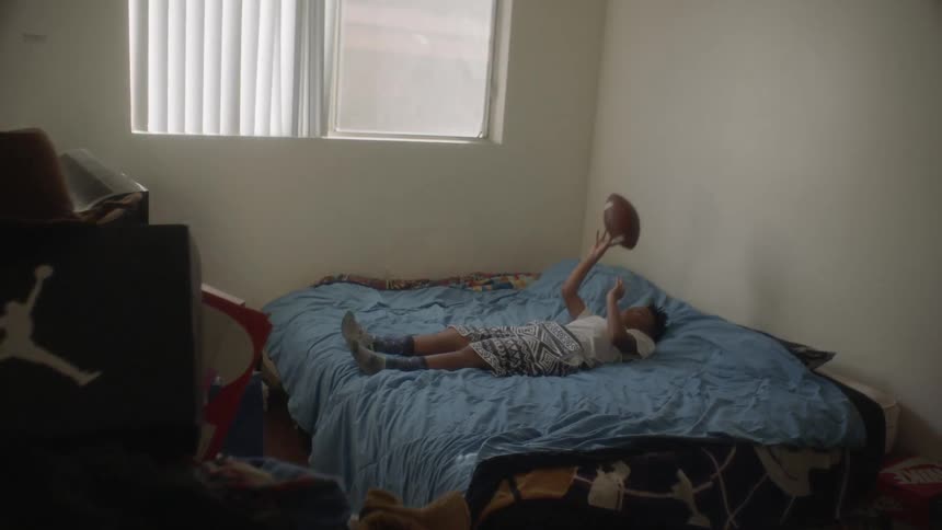 A young boy is lying on his bed and tossing a football during the day