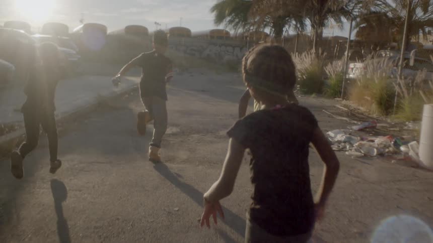 Children run down a street at sunset