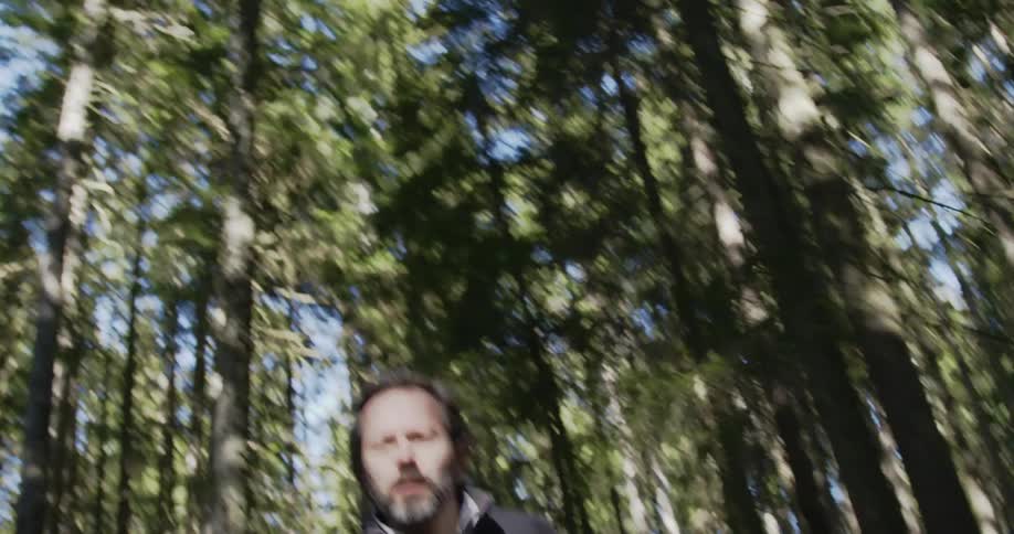 A man looking frightened as he runs through a forest