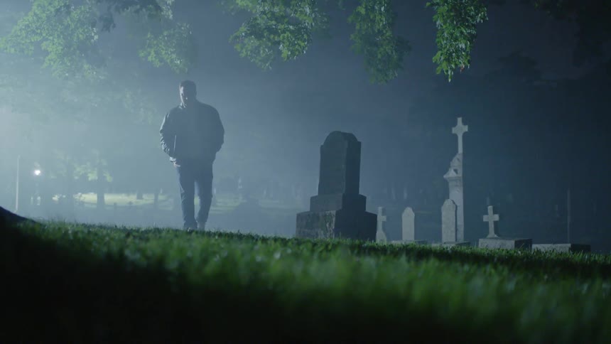 A man walks alone in a cemetery at night