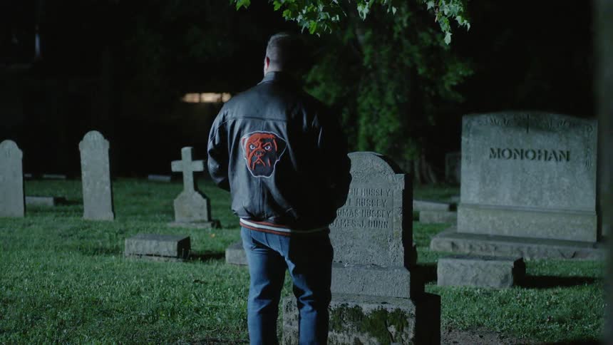 A man looks at a headstone in a cemetery at night