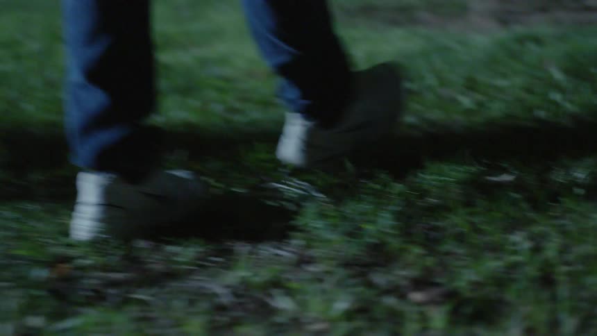 A man is walking toward a gravestone in a cemetery at night