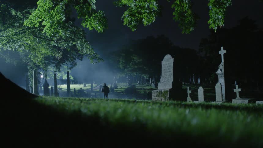 A man is walking through a cemetery at night