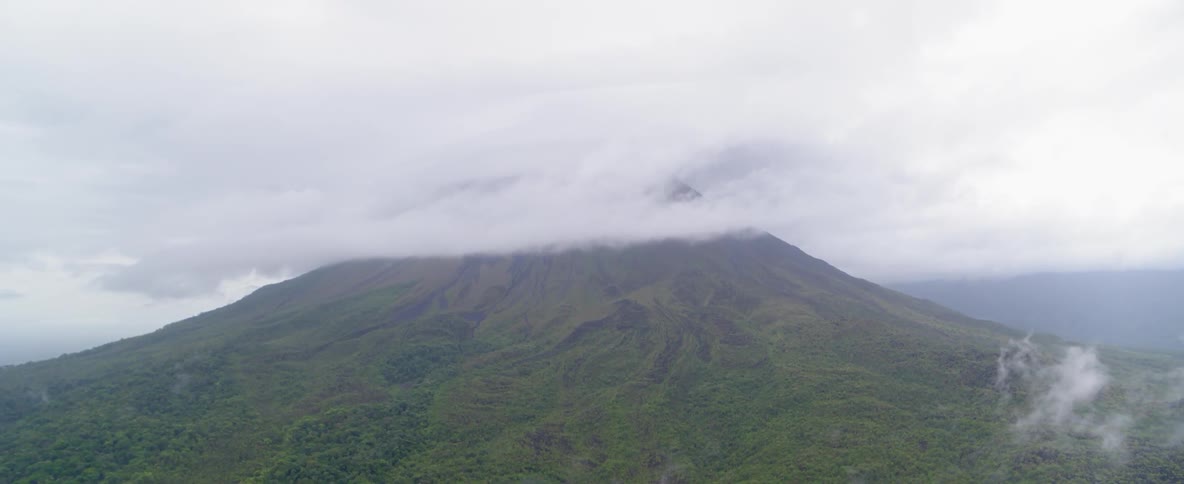 Fog drifts over a tree-covered mountainside on a cloudy day