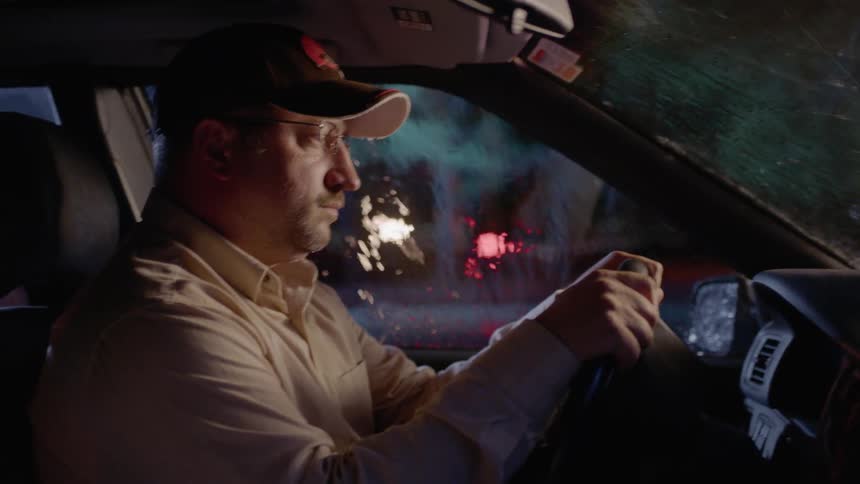 A man sits in a car while it's raining