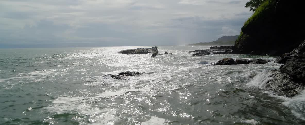 Waves crash over rocks at the base of cliffs during the day