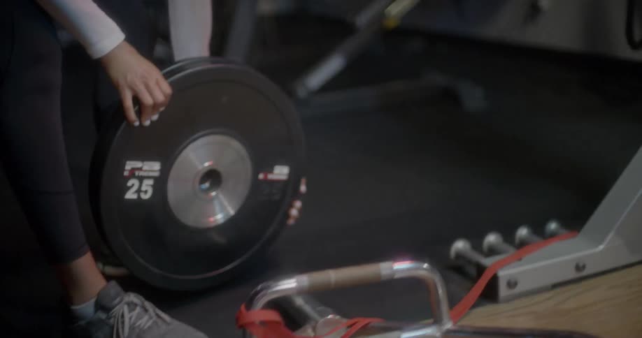 A woman carries a large weight to a bar in a gym
