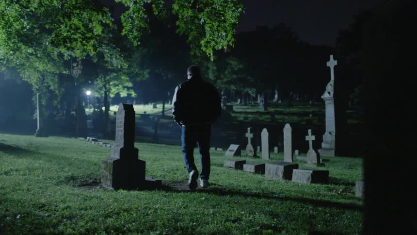 Man walks through a graveyard at night