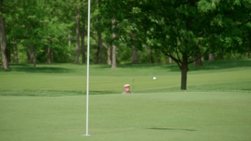 A golfer is taking a shot from a sand trap on a golf course