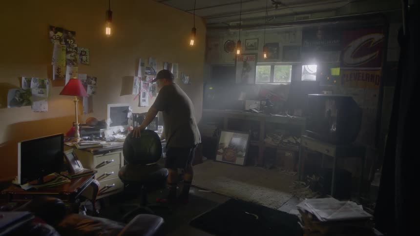 A man stands by an office chair in a garage