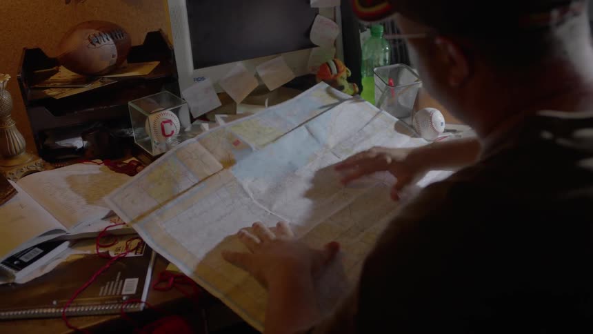 A man is opening up a large piece of paper on a desk and looking at it closely