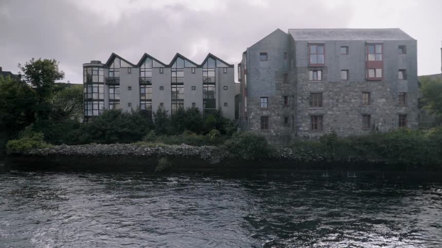 Old buildings are standing next to a choppy river on a cloudy day