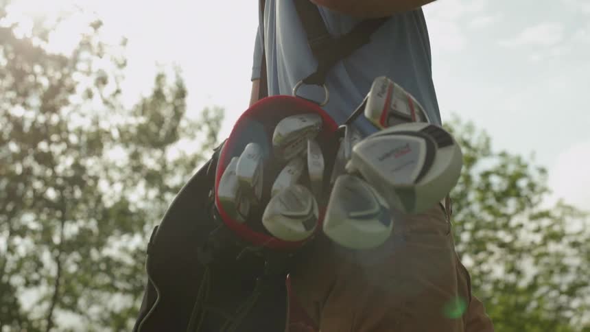 Golf clubs jangle and sway in a golf bag as a golfer carries them